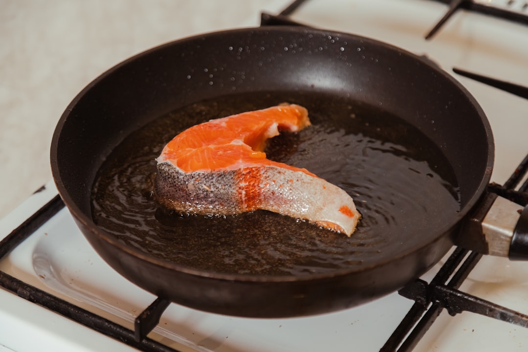 Piece of salmon fish frying on hot pan with sizzling oil at home kitchen